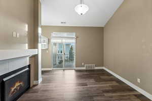 Unfurnished living room with dark wood-type flooring, a lit fireplace, and lofted ceiling