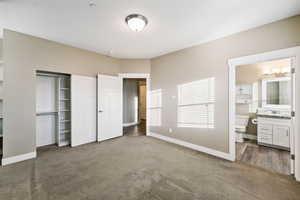 Unfurnished bedroom with a closet, dark colored carpet, and ensuite bathroom