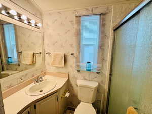 Full bathroom featuring wallpapered walls, vanity, and a shower stall