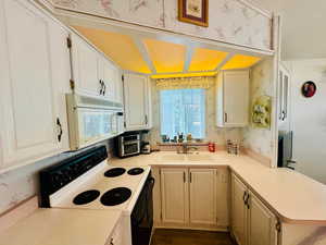 Kitchen featuring wallpapered walls, black electric range, light countertops, white microwave, and white cabinetry