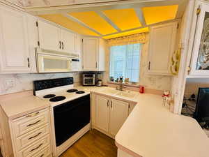 Kitchen featuring range with electric stovetop, light countertops, white microwave, wallpapered walls, and dark wood-type flooring