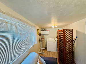 Laundry room featuring a textured ceiling, light wood-style flooring, and washer and clothes dryer