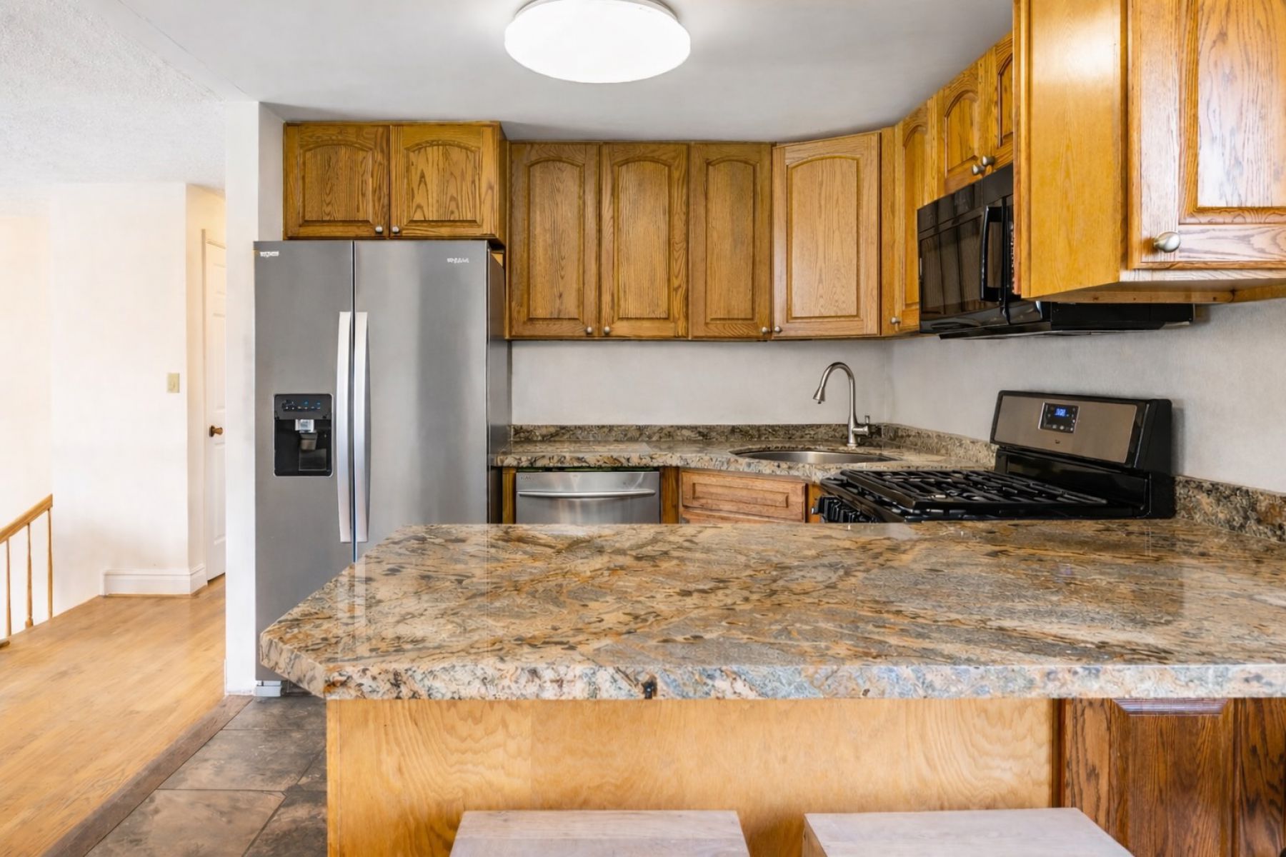 Kitchen featuring stainless steel appliances, wood finish cabinetry, a peninsula, and light stone counters
