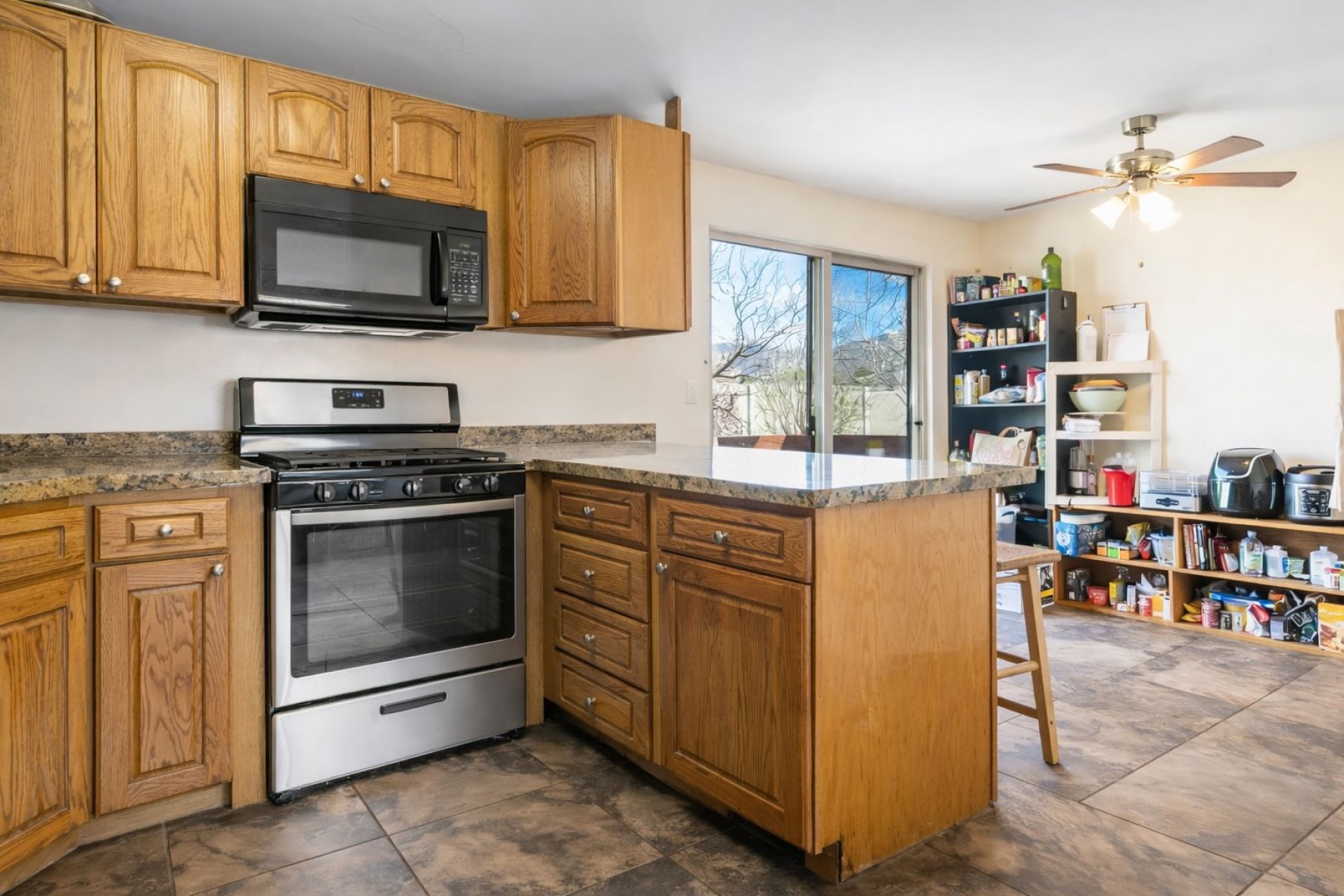Kitchen featuring stainless steel gas range, a peninsula, black microwave, a ceiling fan, and a breakfast bar area