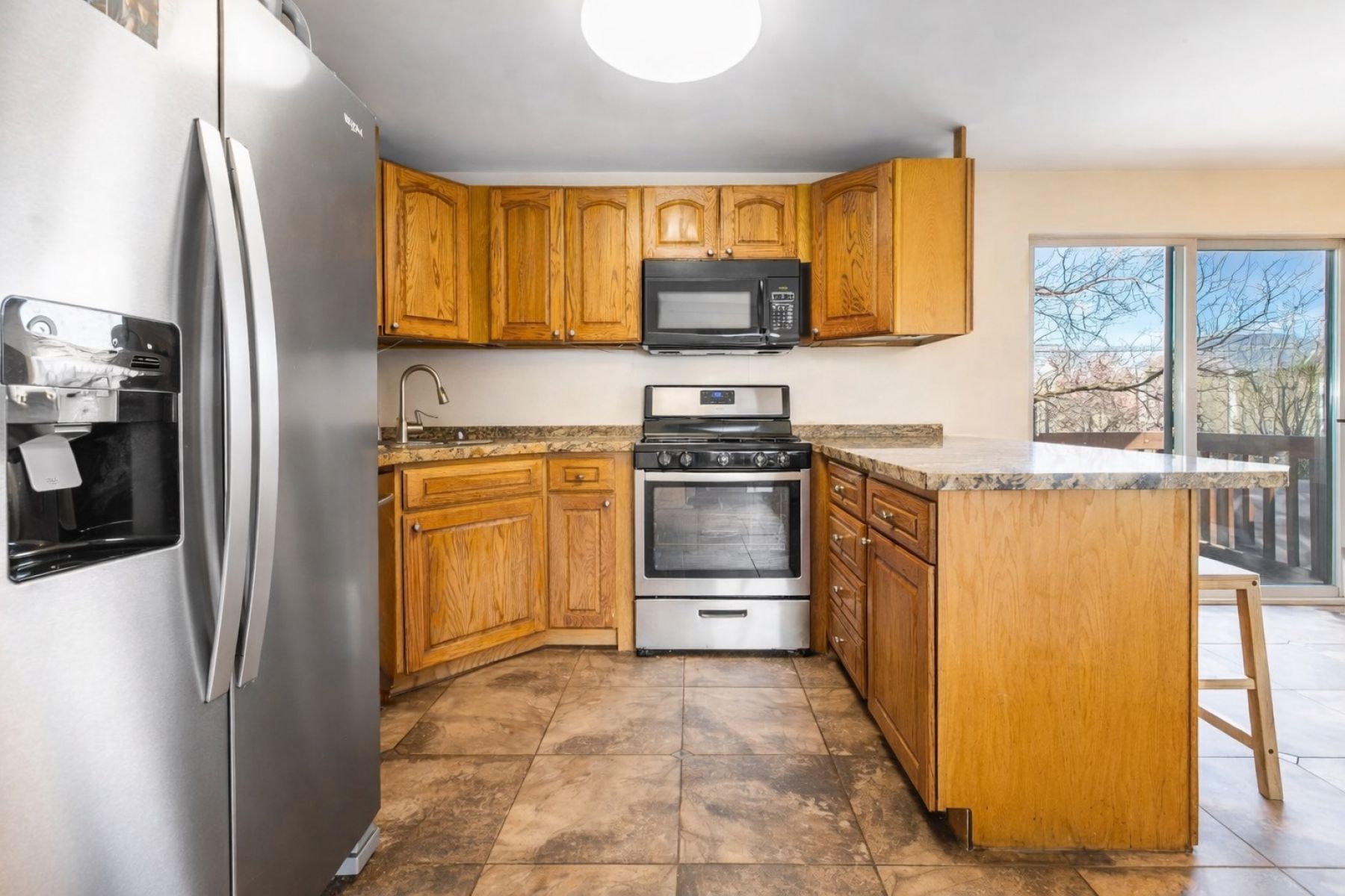 Kitchen with stainless steel appliances, a peninsula, a kitchen bar, and light stone counters