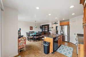 Kitchen with dark countertops, stainless steel appliances, an island with sink, wood finish cabinetry, and a breakfast bar