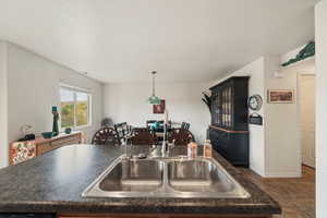 Kitchen featuring dark countertops, a kitchen island with sink, decorative light fixtures, and a textured ceiling