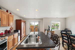 Kitchen featuring dark countertops, a kitchen island with sink, recessed lighting, wood finish cabinetry, and a textured ceiling