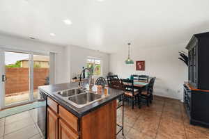 Kitchen with a center island with sink, dark countertops, light tile patterned flooring, black dishwasher, and a breakfast bar area
