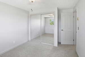 Unfurnished bedroom with a textured ceiling, light carpet, and a closet