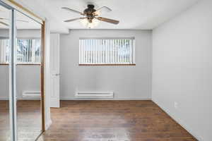 Unfurnished bedroom featuring a closet, dark wood-style flooring, ceiling fan, a baseboard heating unit, and baseboard heating