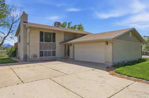 Split level home featuring brick siding, a garage, driveway, and a chimney