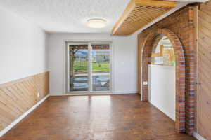 Empty room with wood walls, wainscoting, a textured ceiling, and dark wood-type flooring