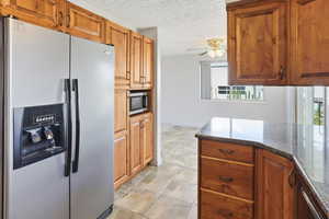 Kitchen with stainless steel appliances, dark stone counters, a textured ceiling, a ceiling fan, and wood finish cabinetry