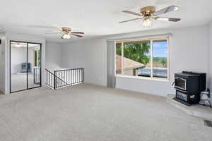 Spare room featuring a ceiling fan, a wood stove, light colored carpet, and a textured ceiling