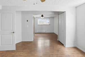 Unfurnished room with ceiling fan, a textured ceiling, dark wood-style flooring, and a baseboard heating unit
