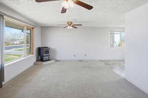 Empty room with a wood stove, light carpet, ceiling fan, and a textured ceiling