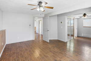 Spare room featuring ceiling fan, a textured ceiling, dark wood-style flooring, and a baseboard heating unit
