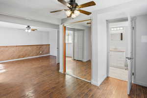 Unfurnished bedroom featuring dark wood-style flooring, a closet, ceiling fan, ensuite bath, and wooden walls