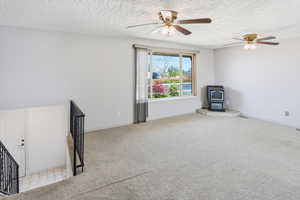 Unfurnished room with a wood stove, ceiling fan, light colored carpet, and a textured ceiling