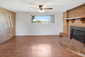 Unfurnished living room featuring wooden walls, dark wood-type flooring, a fireplace, ceiling fan, and a textured ceiling