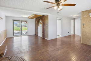 Empty room with a textured ceiling, dark wood-style floors, and a ceiling fan