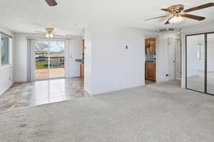 Unfurnished living room with a ceiling fan, light colored carpet, a textured ceiling, and light tile patterned floors