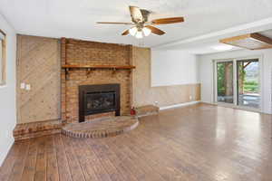Unfurnished living room with wooden walls, a ceiling fan, a fireplace, hardwood / wood-style flooring, and a textured ceiling
