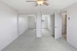 Unfurnished bedroom with two closets, light colored carpet, a textured ceiling, and ceiling fan
