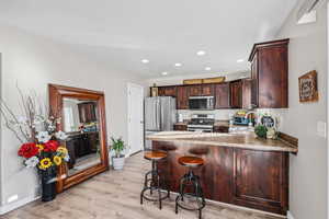 Kitchen with a peninsula, stainless steel appliances, a breakfast bar area, dark wood finish cabinets, and light wood-style flooring