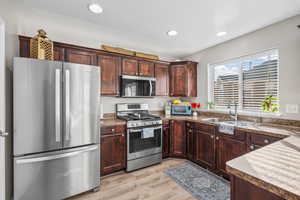 Kitchen featuring stainless steel appliances, dark wood finish cabinetry, light wood finished floors, recessed lighting, and dark countertops