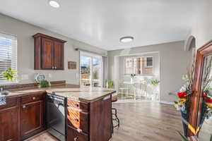 Kitchen with a peninsula, dishwasher, light wood-style flooring, a kitchen breakfast bar, and dark countertops