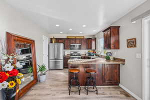 Kitchen featuring stainless steel appliances, a peninsula, a kitchen bar, recessed lighting, and dark wood finish cabinets
