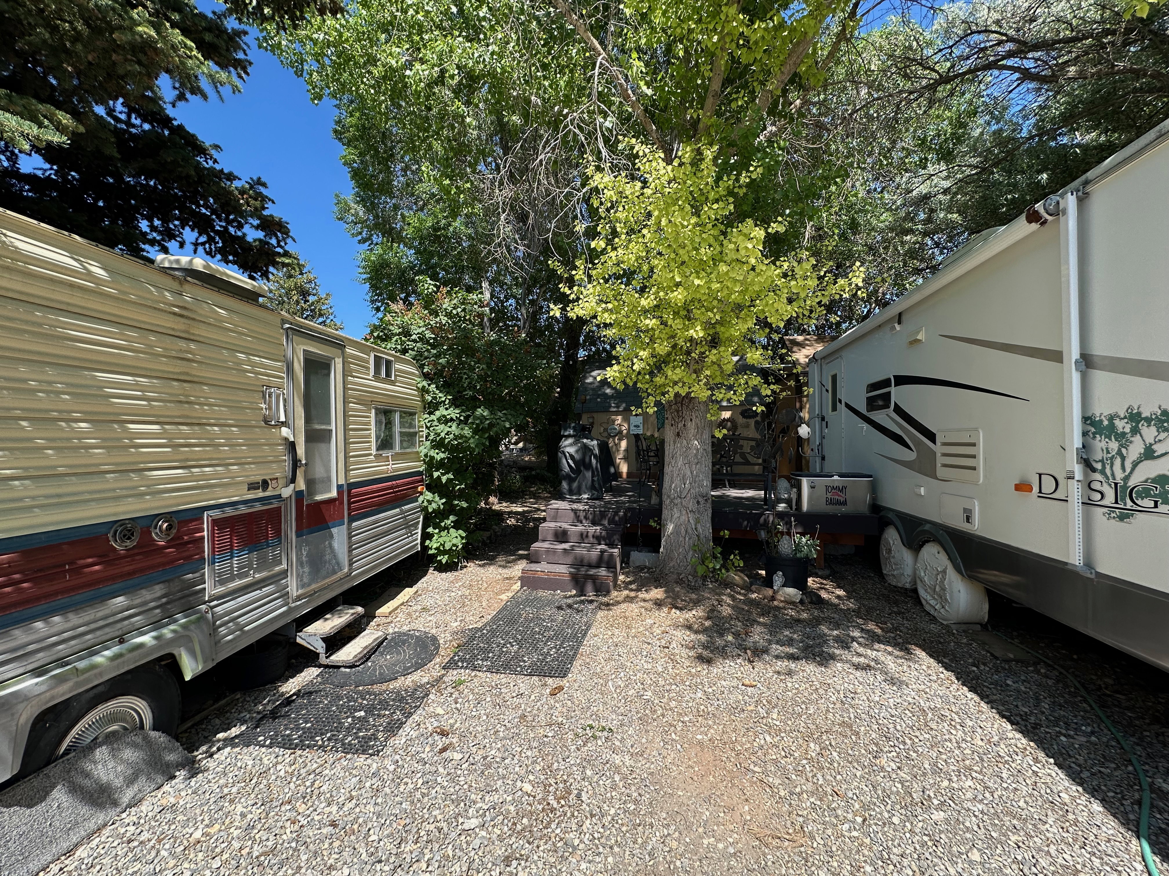 Gravel lot featuring mature trees and two recreational vehicles