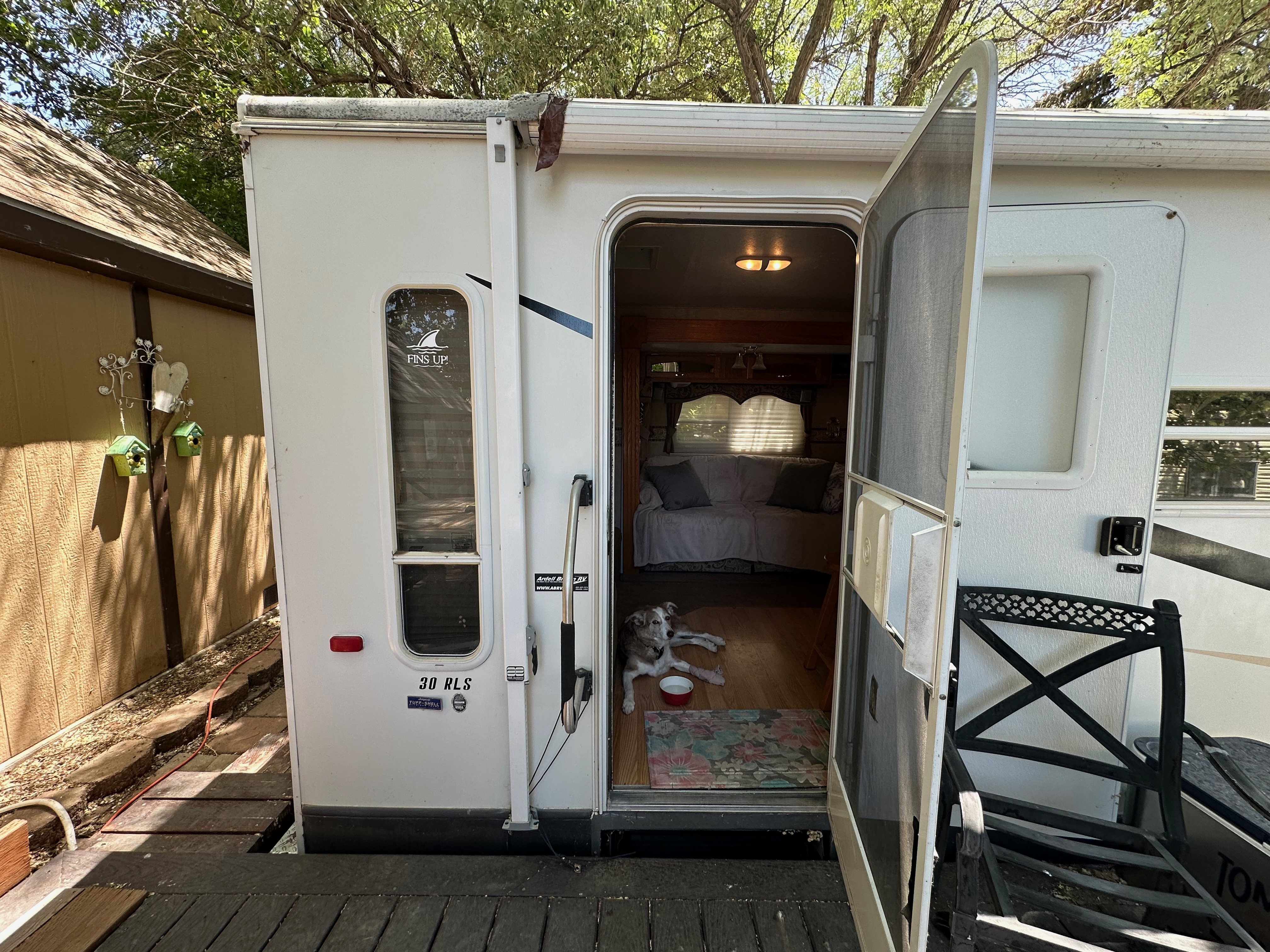 Recreational vehicle entry featuring a screen door, wood-finish flooring, and an interior with a sofa and window treatments