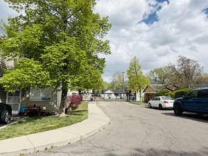 View of asphalt road featuring sidewalks, a residential view, a gate, and curbs