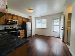 Kitchen with dark countertops, stainless steel appliances, a textured ceiling, wood finish cabinetry, and dark wood-type flooring