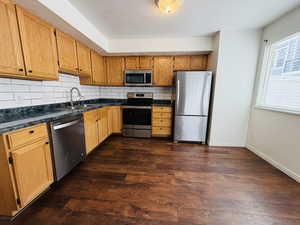 Kitchen featuring stainless steel appliances, decorative backsplash, dark wood-style floors, and wood finish cabinets