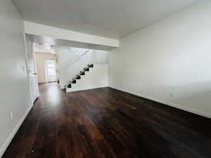 Unfurnished living room with stairs and dark wood-style flooring