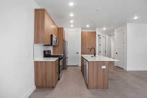 Kitchen featuring concrete flooring, stainless steel appliances, a kitchen island with sink, wood finish cabinetry, and recessed lighting