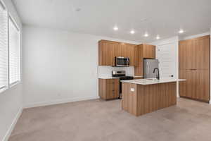 Kitchen with modern cabinets, stainless steel appliances, a center island with sink, and recessed lighting