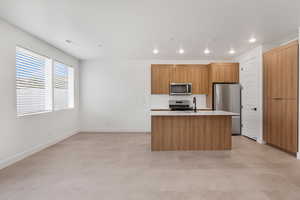 Kitchen with modern cabinets, stainless steel appliances, a center island with sink, light stone countertops, and tasteful backsplash