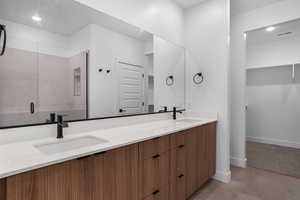 Bathroom with a spacious closet, double vanity, recessed lighting, and a stall shower