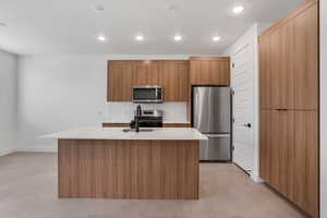 Kitchen featuring modern cabinets, finished concrete floors, stainless steel appliances, a kitchen island with sink, and wood finish cabinetry