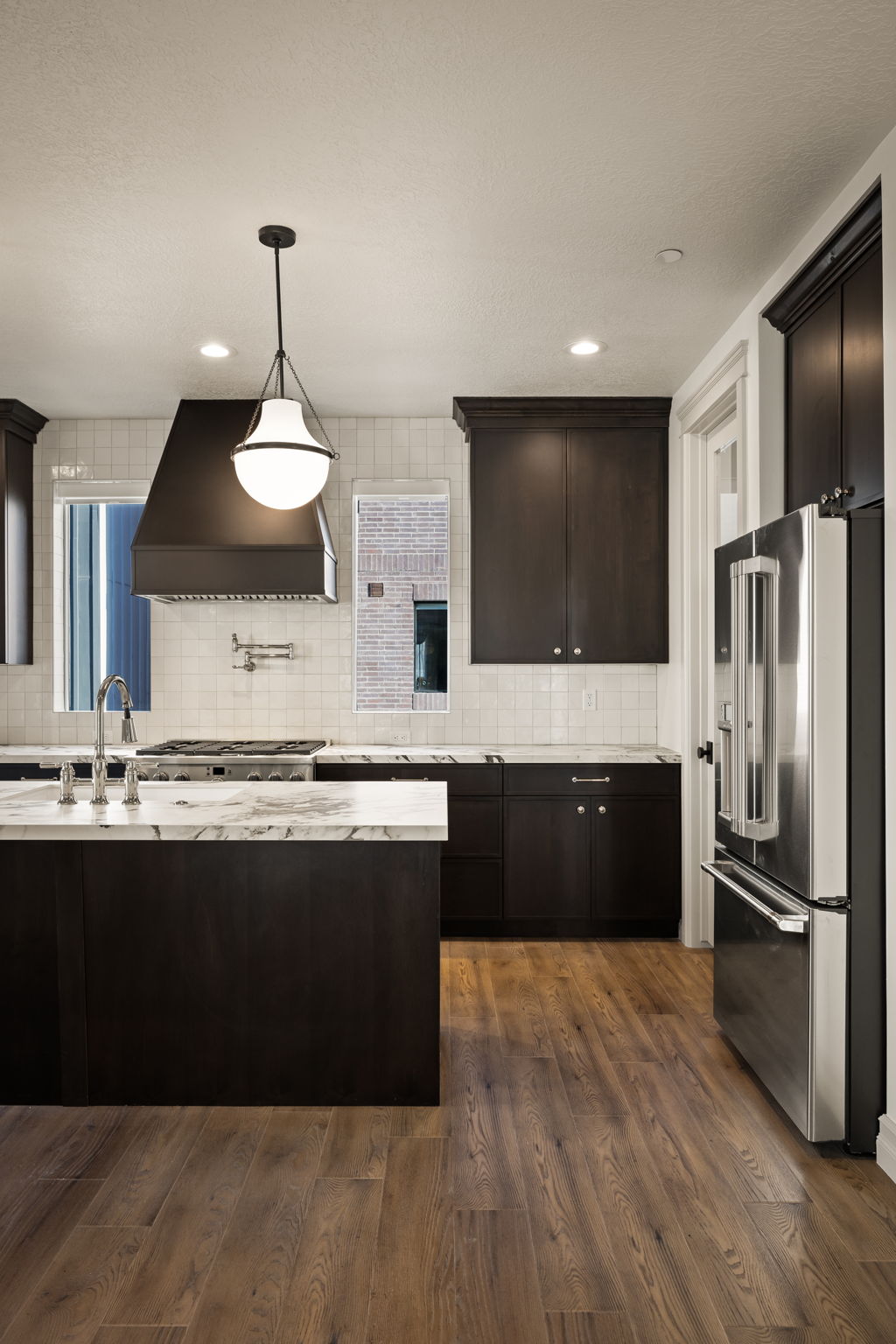 Pictures of an exterior unit -Kitchen featuring high end fridge, dark wood finish cabinets, dark wood-style flooring, light stone counters, and backsplash