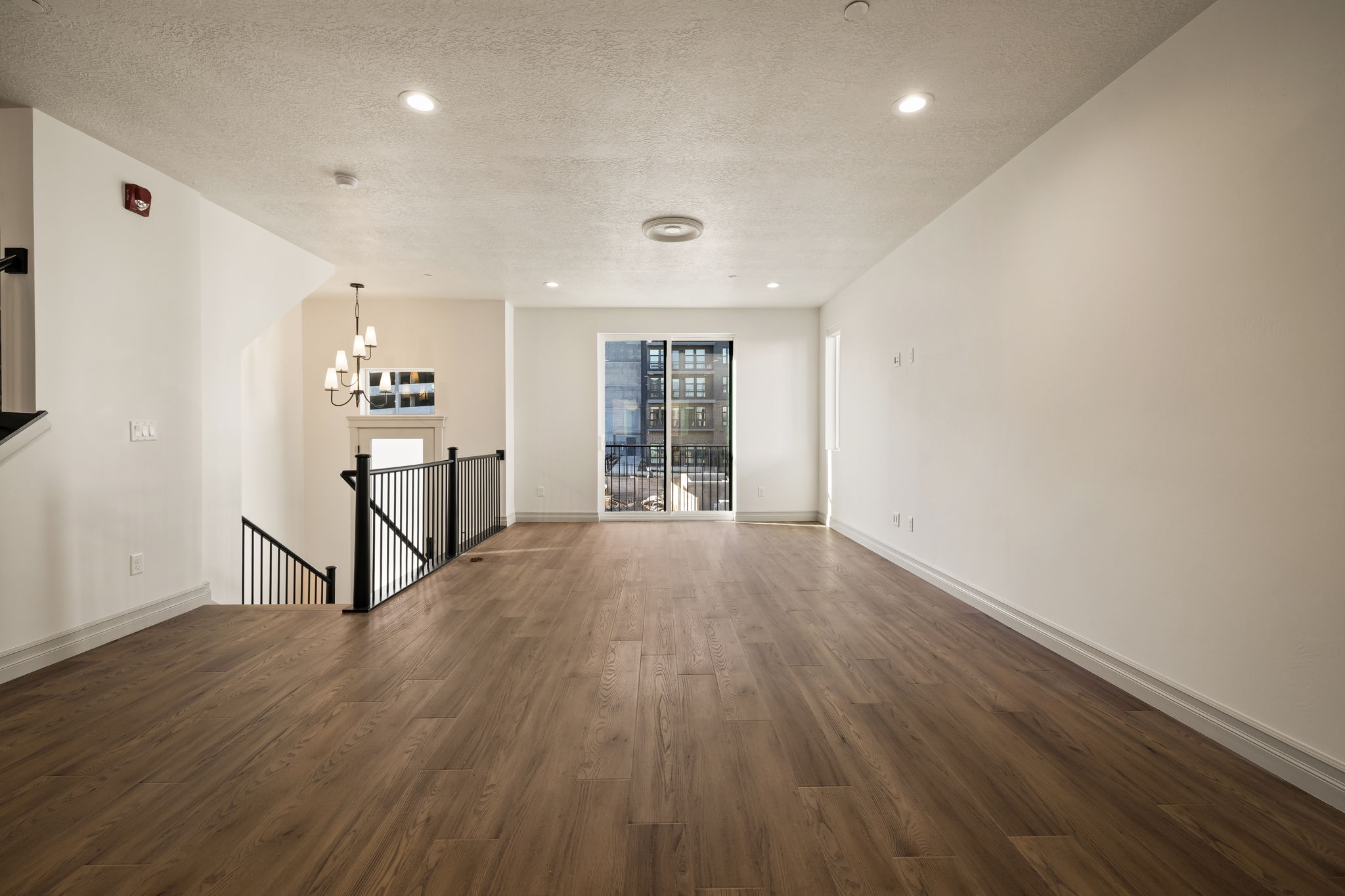 Photos of an exterior unit with the same finishes -Unfurnished living room featuring dark wood-style flooring, a textured ceiling, and a chandelier