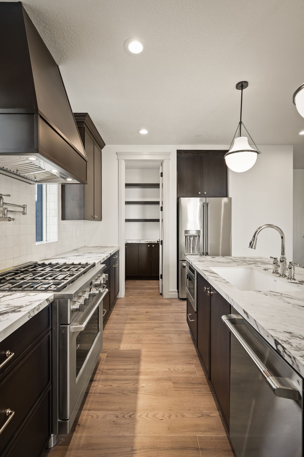 Photos of an exterior unit with the same finishes -Kitchen featuring high end appliances, light stone countertops, light wood-style flooring, decorative backsplash, and dark wood finish cabinetry