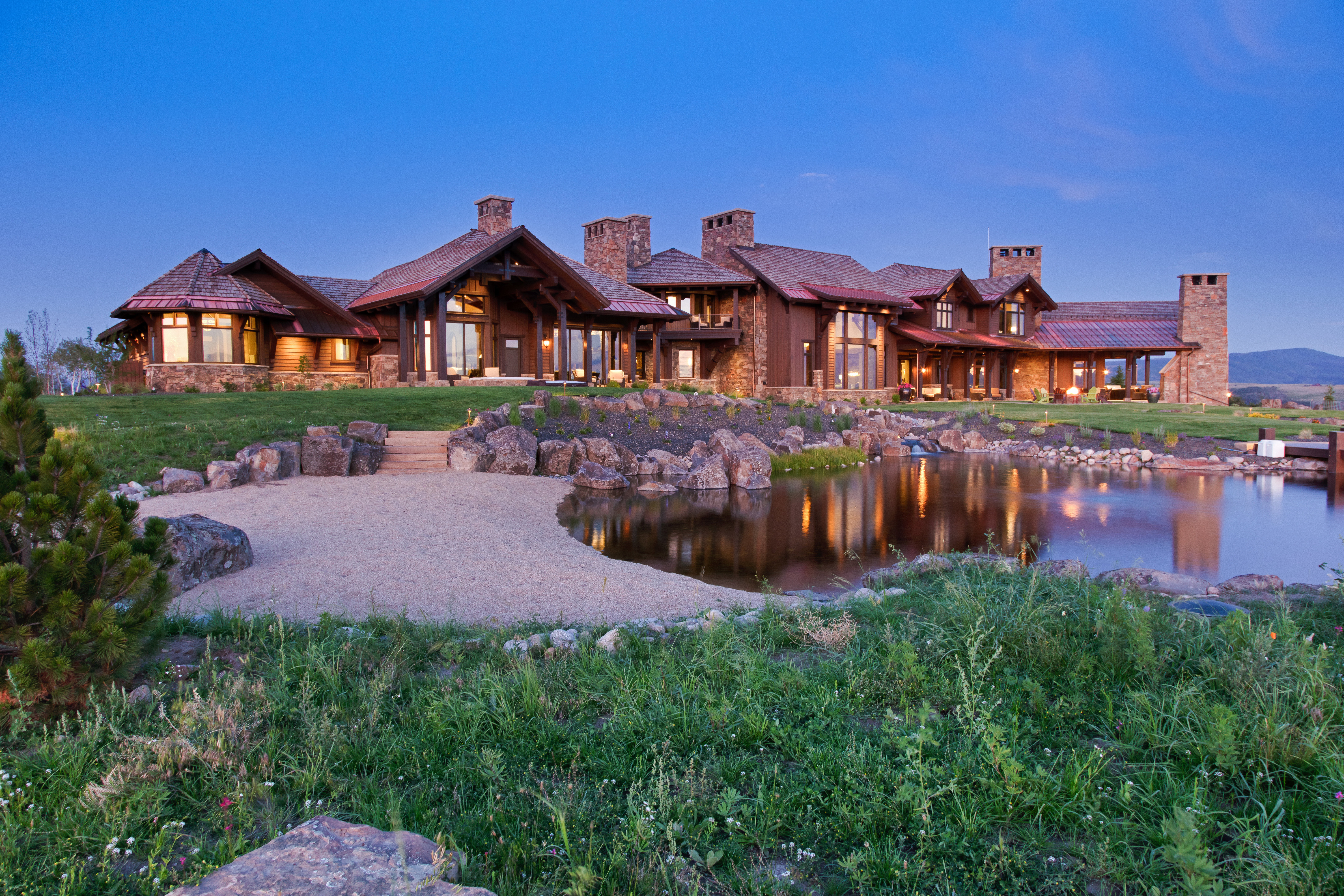Back of property at dusk featuring a chimney, stone siding, a lawn, and a water view