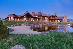 Back of property at dusk featuring a chimney, stone siding, a lawn, and a water view
