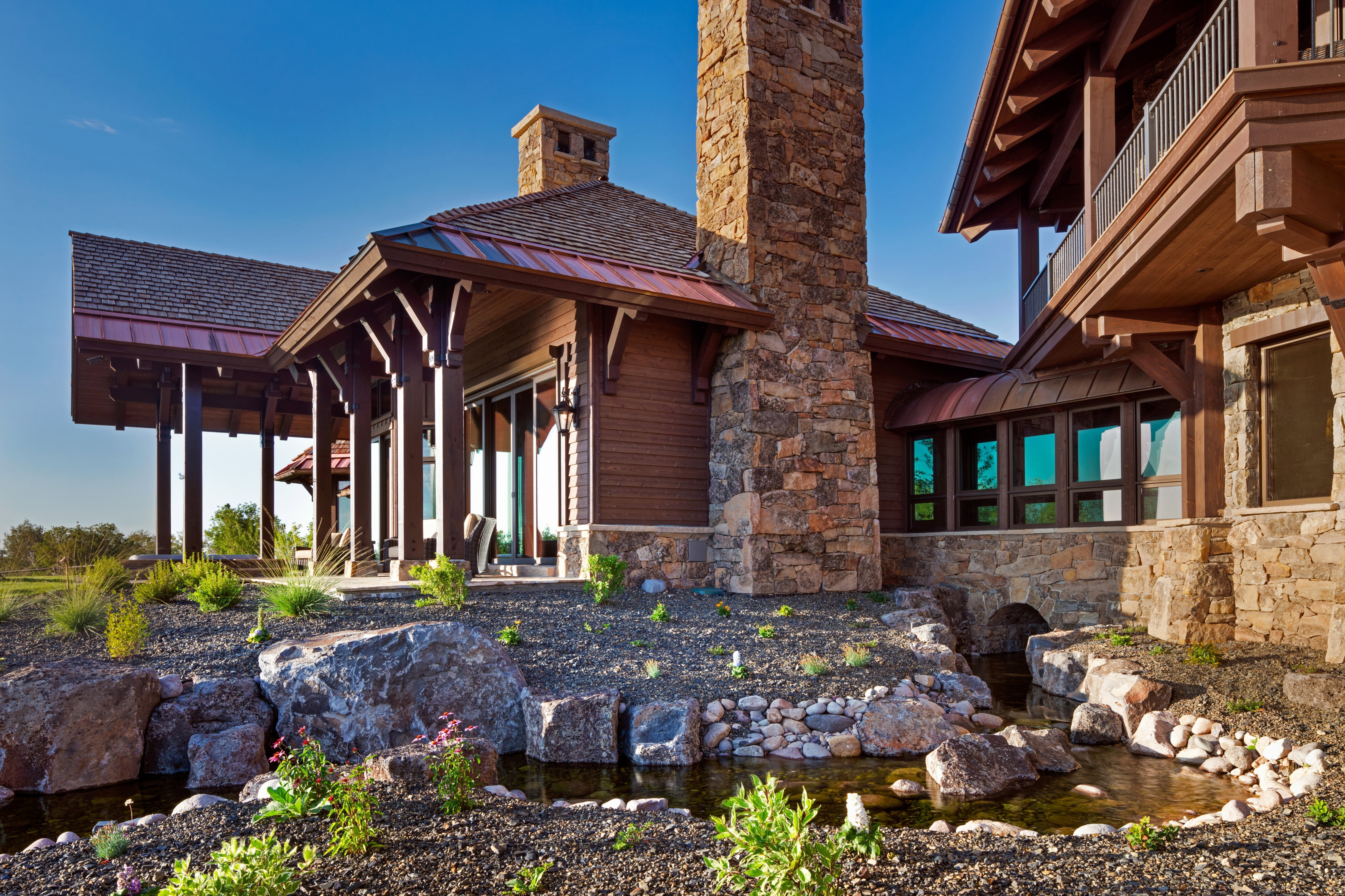 Back of property with a garden pond, a standing seam roof, a chimney, stone siding, and a porch